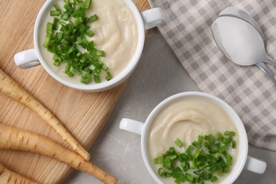 Photo of Bowls with tasty creamy soup of parsnip served on light grey table, flat lay