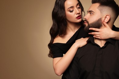 Handsome bearded man with sexy lady on light brown background. Space for text
