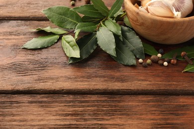 Photo of Aromatic fresh bay leaves and spices on wooden table, space for text