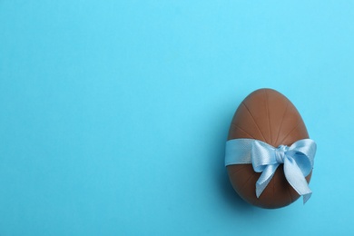 Photo of Sweet chocolate egg with bow on light blue background, top view. Space for text