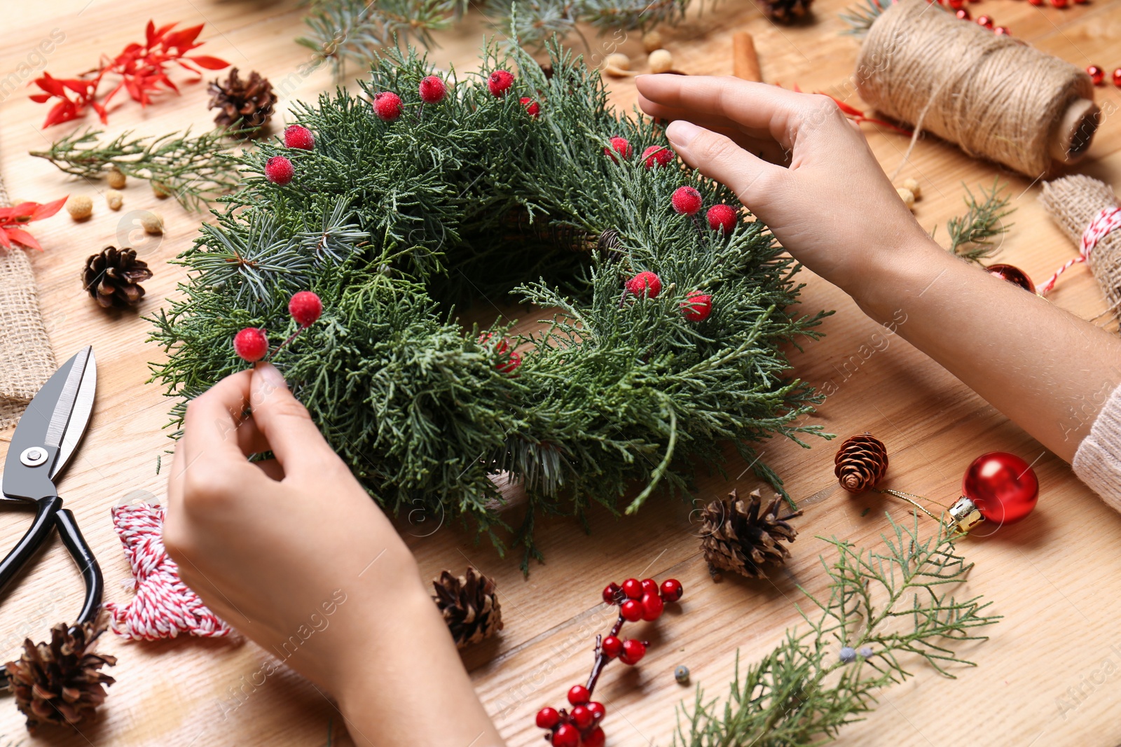 Photo of Florist making beautiful Christmas wreath with berries at wooden table, closeup