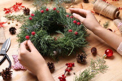 Florist making beautiful Christmas wreath with berries at wooden table, closeup