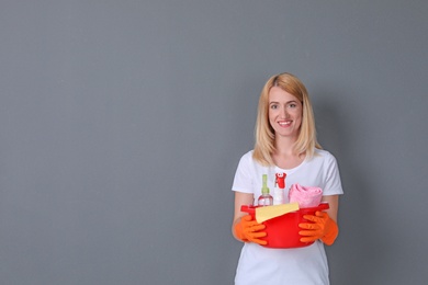 Woman with cleaning supplies on grey background