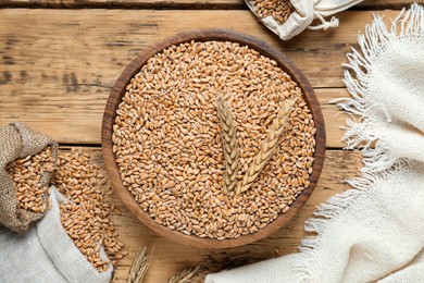 Photo of Bowl of wheat grains and spikes on wooden table, flat lay