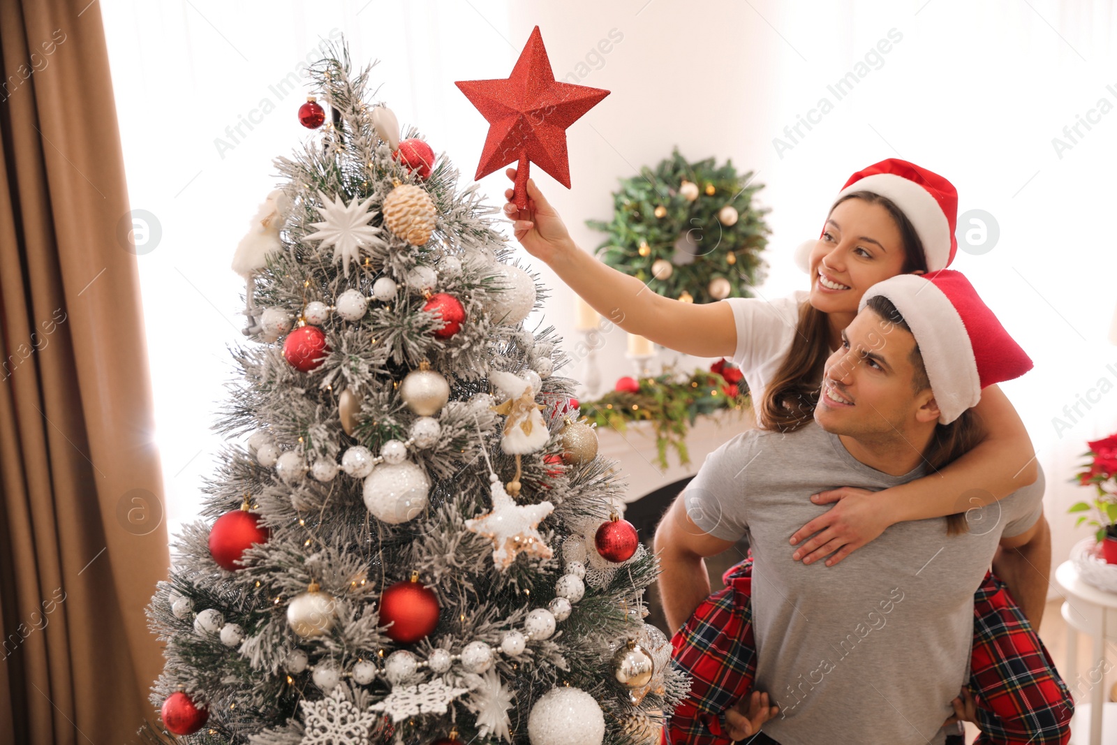 Photo of Couple decorating Christmas tree with star topper indoors