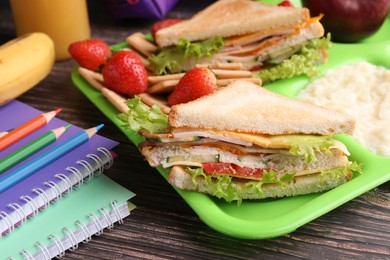 Photo of Serving tray of healthy food and stationery on wooden table, closeup. School lunch