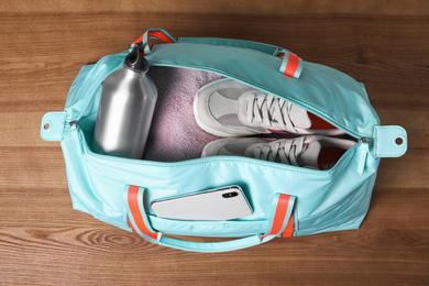 Photo of Open sports bag full of gym stuff on wooden background, top view