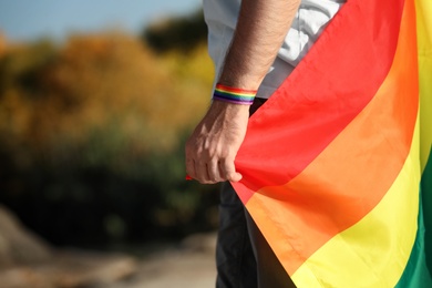 Photo of Man with rainbow LGBT flag as gay symbol outdoors, closeup. Space for text