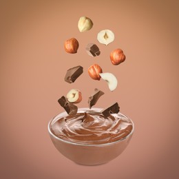 Image of Making yummy chocolate paste. Hazelnuts and pieces of chocolate falling into bowl on light brown background