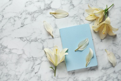 Photo of Beautiful lilies with notebook on marble background, top view. Space for text