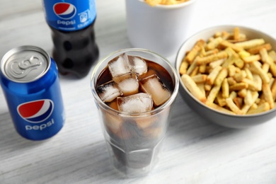 MYKOLAIV, UKRAINE - FEBRUARY 15, 2021: Glass of Pepsi, can and snack on white wooden table