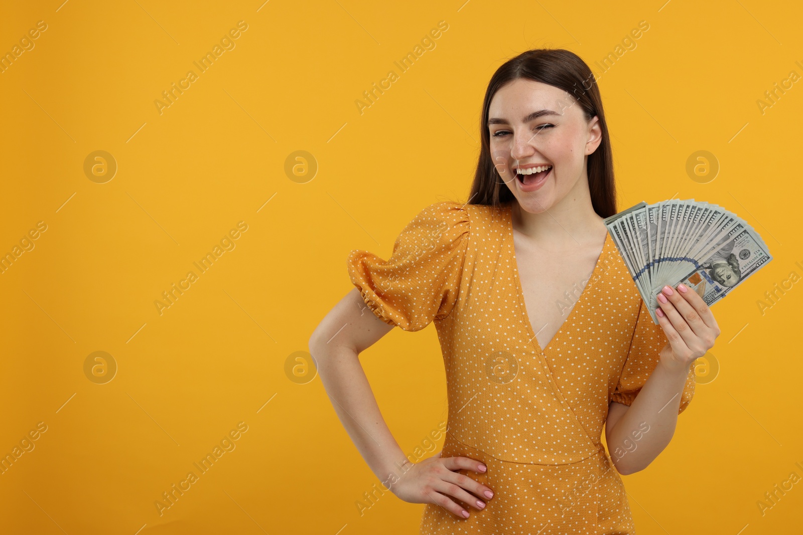 Photo of Happy woman with dollar banknotes on orange background, space for text