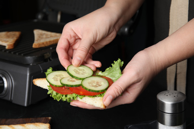 Photo of Woman adding cucumber to sandwich at black table, closeup