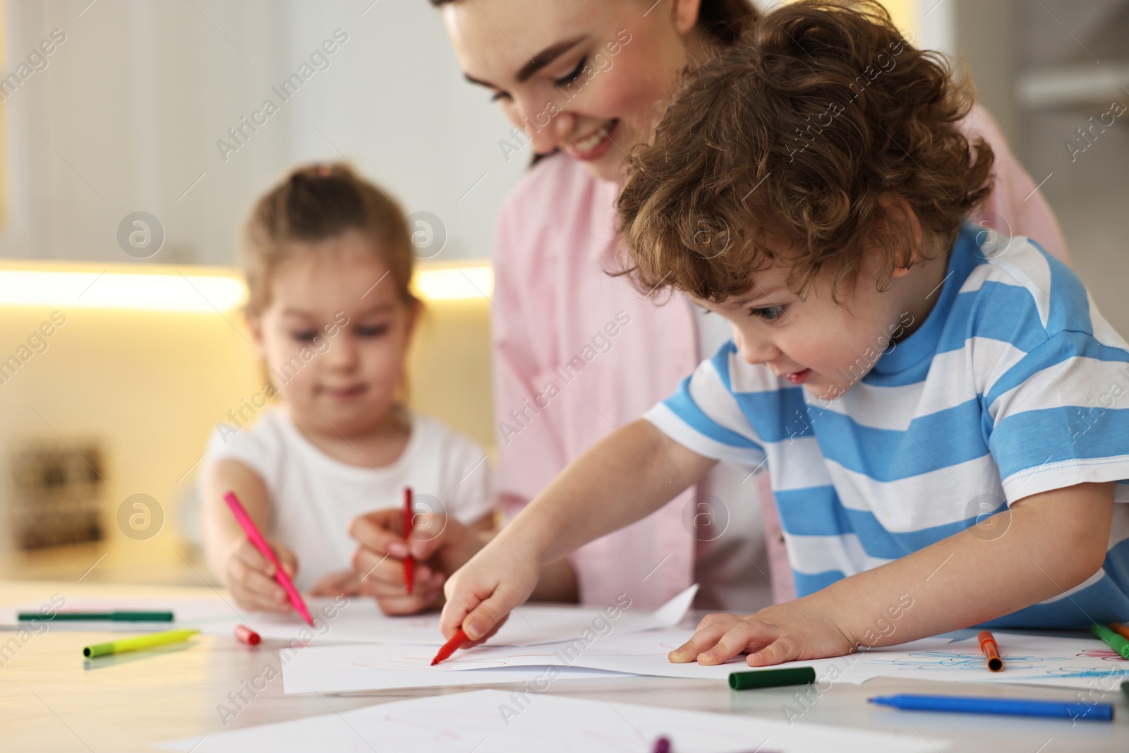 Photo of Mother and her little children drawing with colorful markers at table in kitchen, selective focus