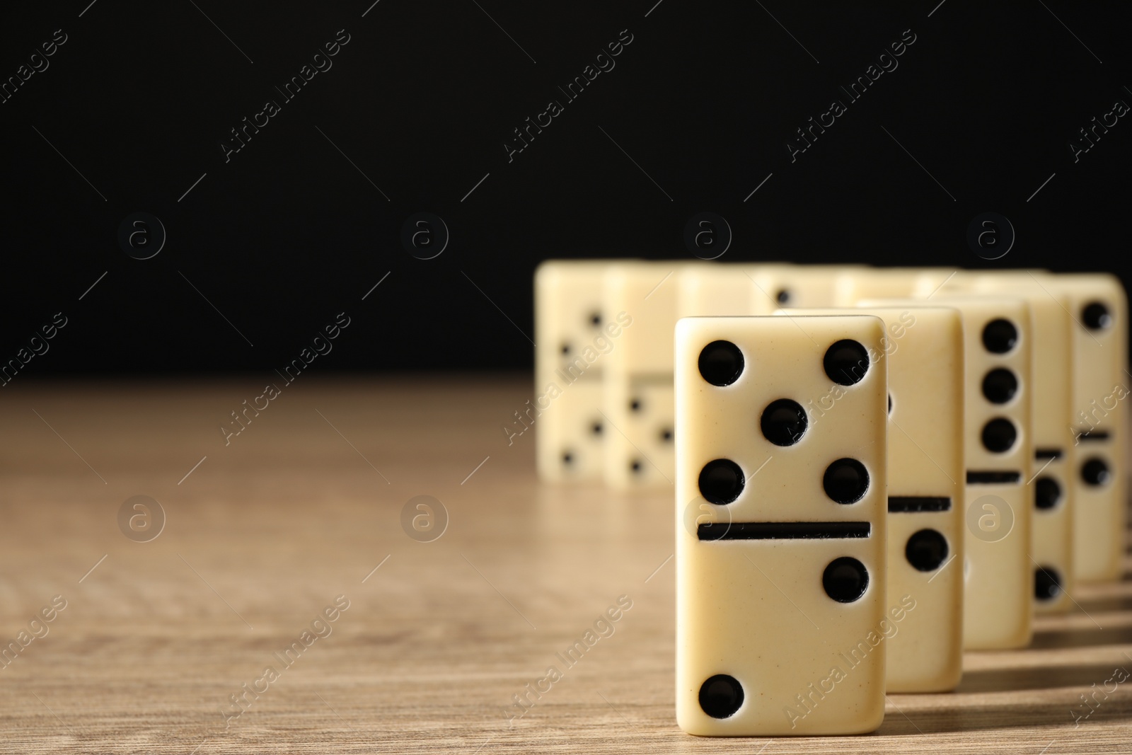 Photo of Domino tiles on wooden table against black background, closeup. Space for text