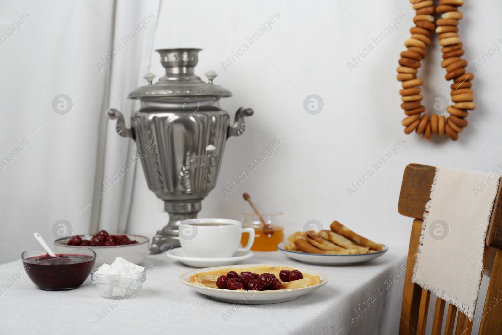 Photo of Vintage samovar, cup of hot drink and snacks served on table indoors. Traditional Russian tea ceremony