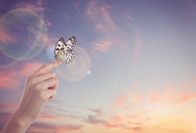 Image of Woman holding beautiful rice paper butterfly against sunset sky, closeup