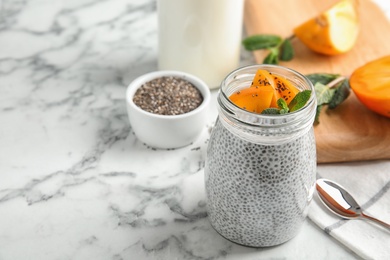 Photo of Jar of tasty chia seed pudding with persimmon and ingredients on table. Space for text