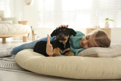 Little girl with cute puppy lying on soft pillow at home