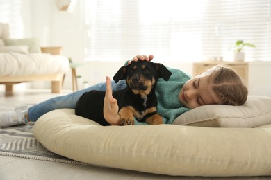 Photo of Little girl with cute puppy lying on soft pillow at home