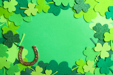 Photo of Frame made of clover leaves and horseshoe on green background, flat lay with space for text. St. Patrick's day