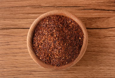 Photo of Dry rooibos leaves in bowl on wooden table, top view