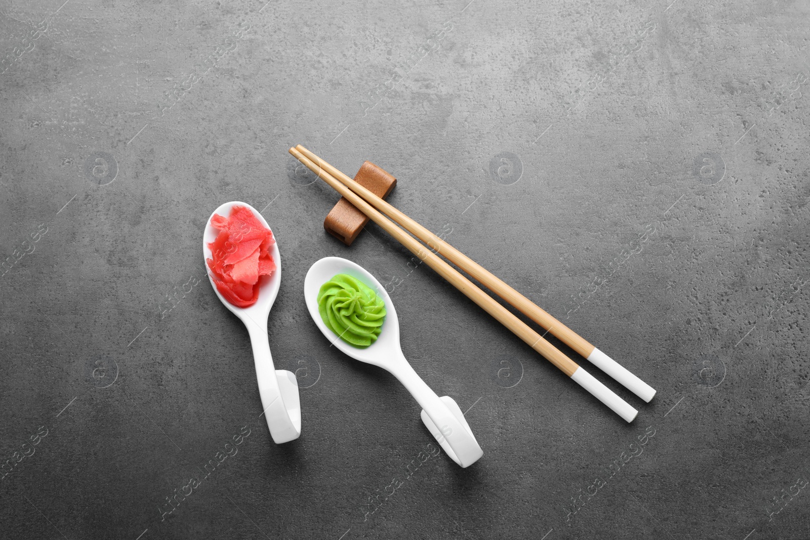 Photo of Swirl of wasabi paste, pickled ginger and chopsticks on grey table, flat lay