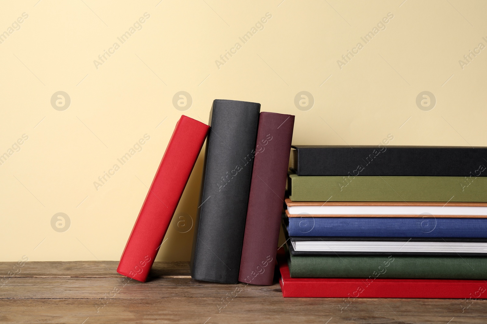 Photo of Many hardcover books on wooden table near yellow wall, space for text