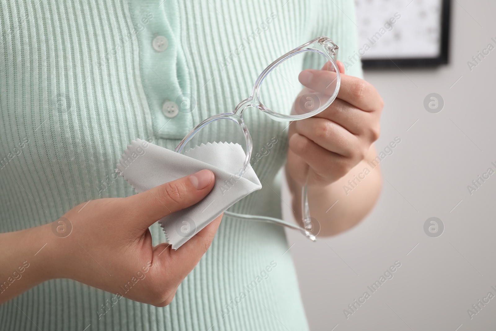 Photo of Woman wiping her glasses with microfiber cloth indoors, closeup