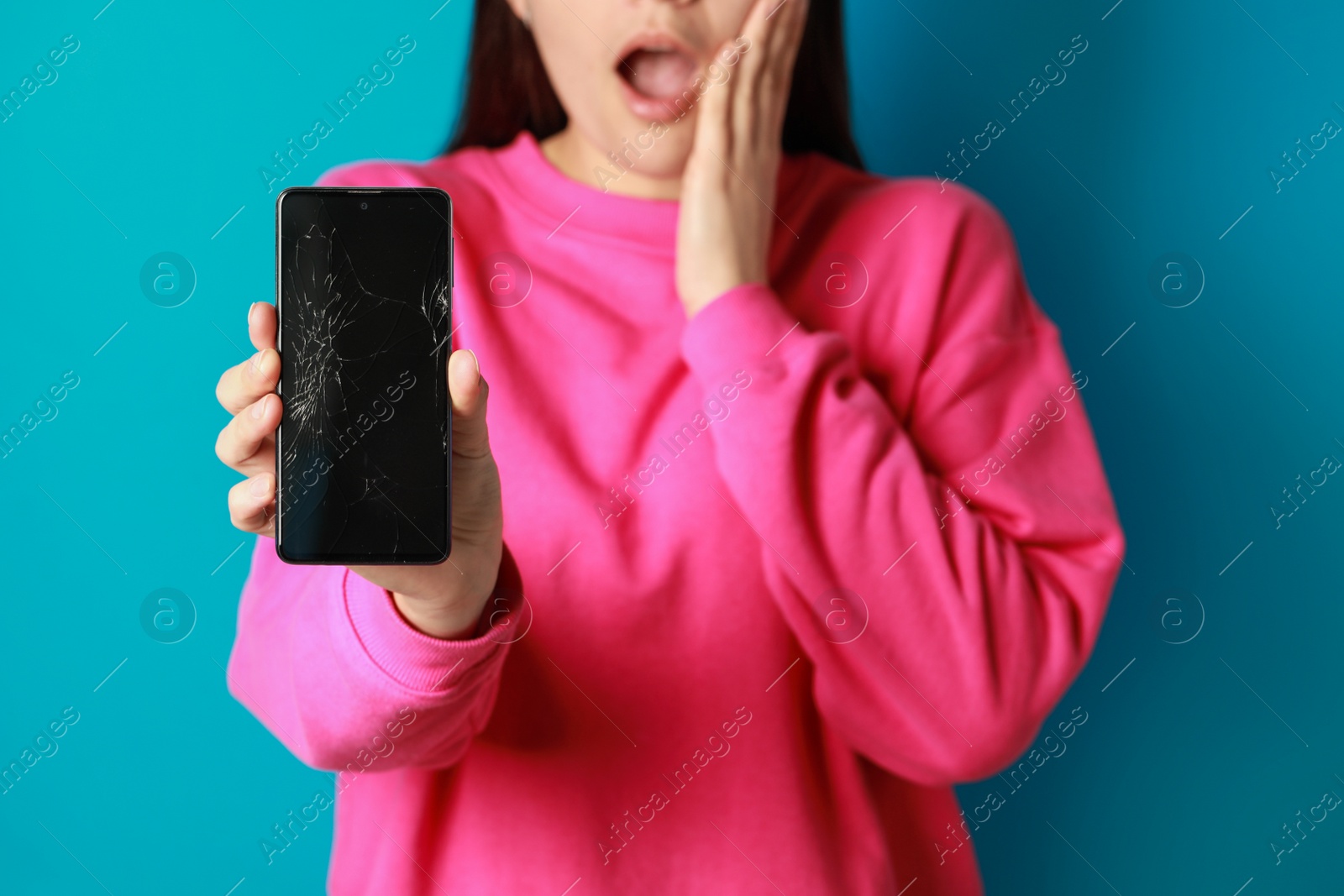 Photo of Shocked woman showing damaged smartphone on light blue background, closeup. Device repairing