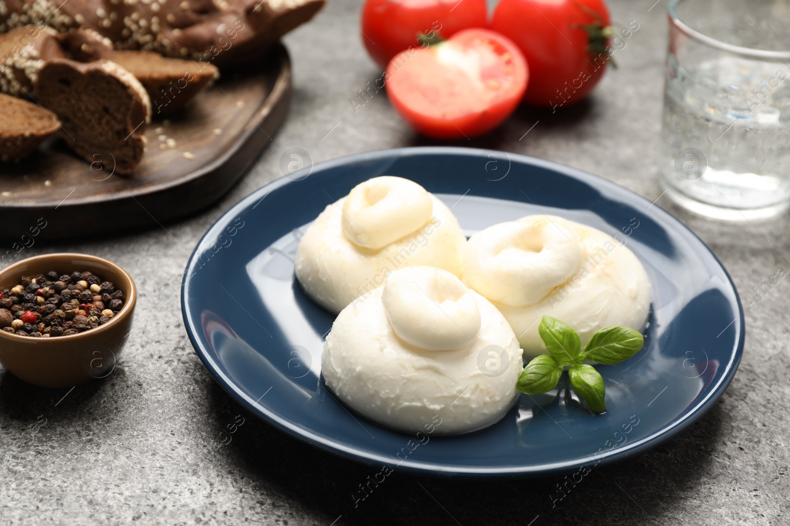 Photo of Delicious burrata cheese with basil on grey table