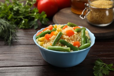 Delicious bulgur with vegetables in bowl on wooden table, closeup