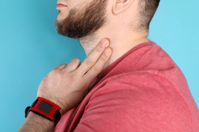 Young man checking pulse on neck against color background, closeup