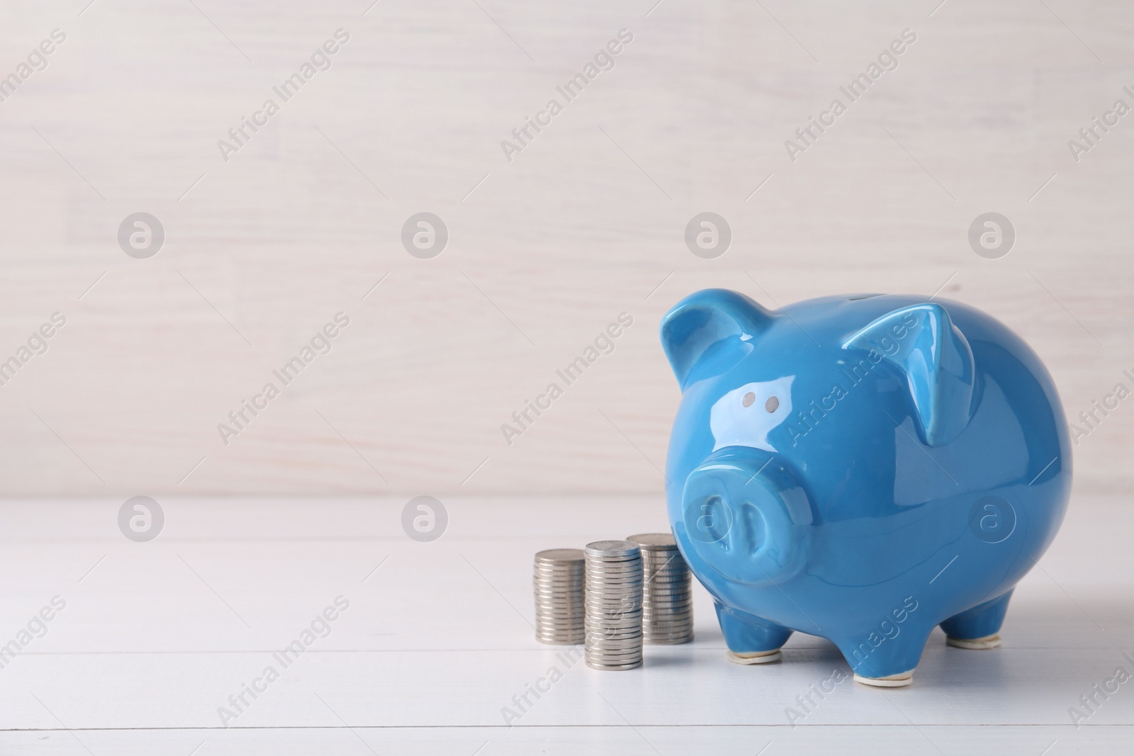 Photo of Financial savings. Piggy bank and stacked coins on white wooden table, space for text