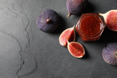 Photo of Glass jar with tasty sweet jam and fresh figs on grey textured table, flat lay. Space for text