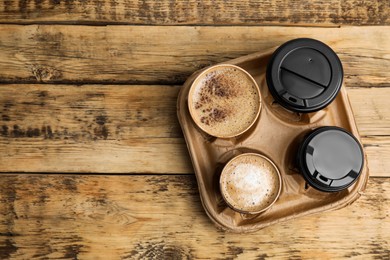 Takeaway paper coffee cups in cardboard holder on wooden table, top view. Space for text