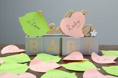 Photo of Cubes with word Baby and paper stickers with different names on wooden table. Choosing baby's name
