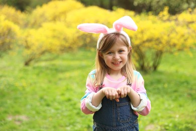 Photo of Easter celebration. Cute little girl with bunny ears outdoors, space for text