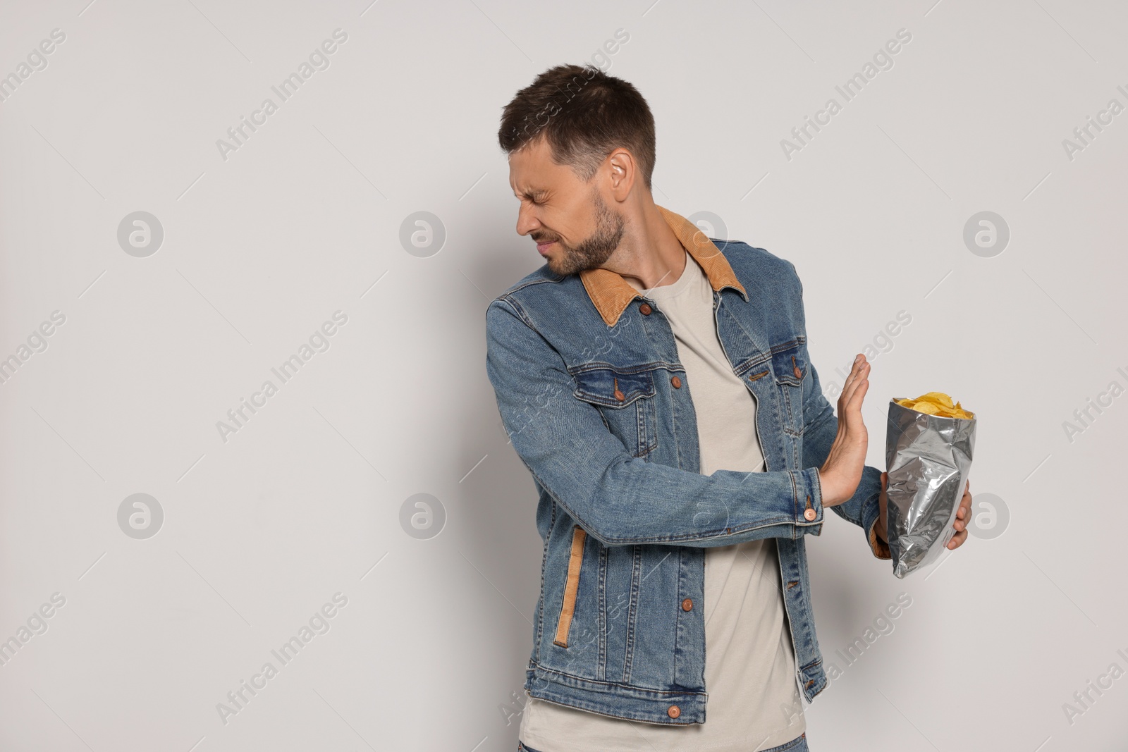 Photo of Handsome man refusing to eat potato chips on light grey background, space for text