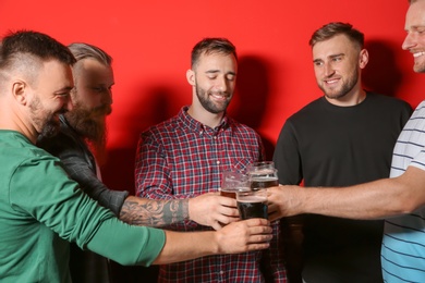 Group of friends clinking glasses with beer on color background
