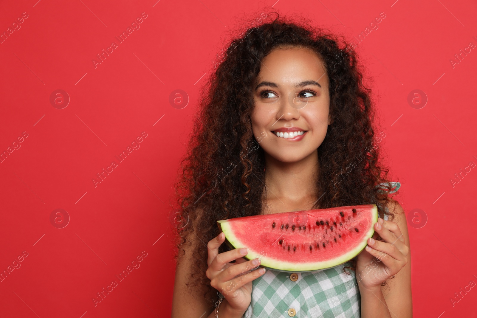 Photo of Beautiful young African American woman with slice of watermelon on red background. Space for text