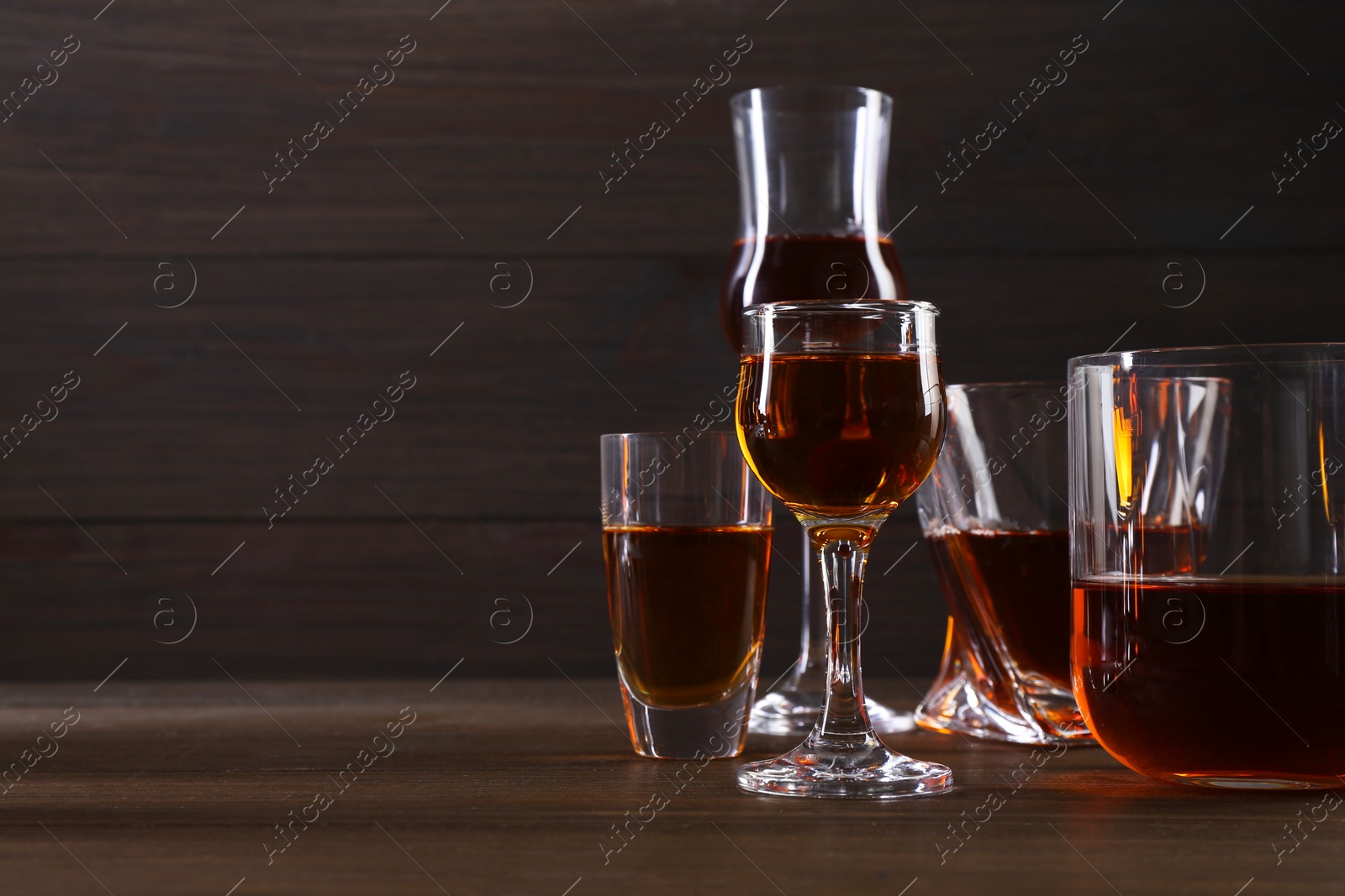 Photo of Different delicious liqueurs in glasses on wooden table, space for text