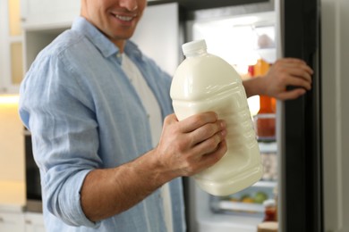 Man with gallon of milk near refrigerator in kitchen, closeup