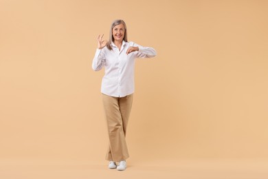 Happy senior woman showing ok gesture on beige background