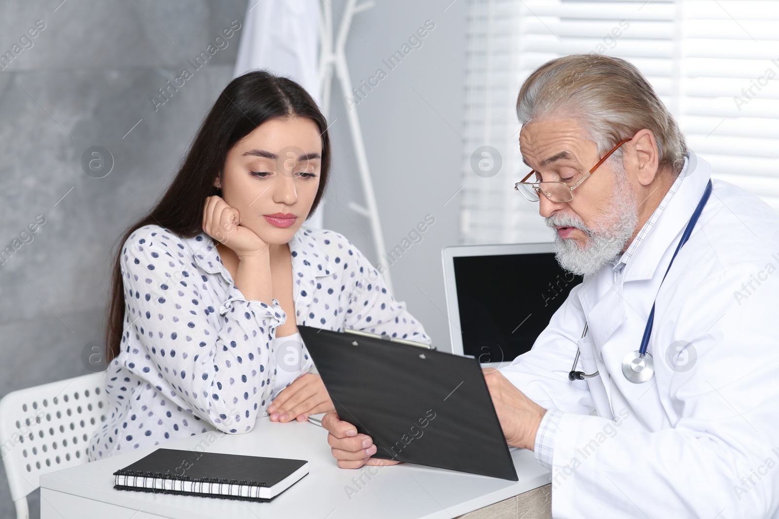 Photo of Senior doctor consulting patient at white table in clinic