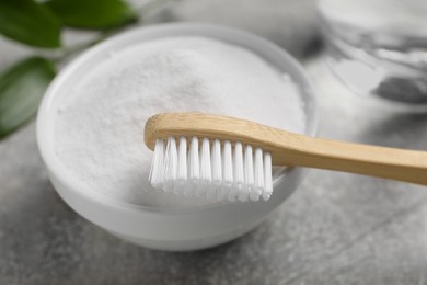 Bamboo toothbrush, green leaf and bowl of baking soda on grey table, closeup