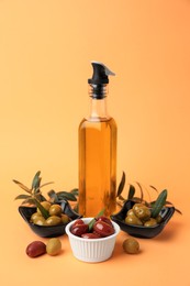Photo of Bottle of oil, olives and tree twigs on orange background