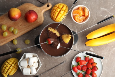 Photo of Flat lay composition with chocolate fondue in pot and fruits on gray background