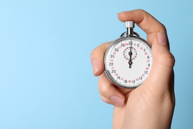 Woman holding vintage timer on light blue background, closeup. Space for text