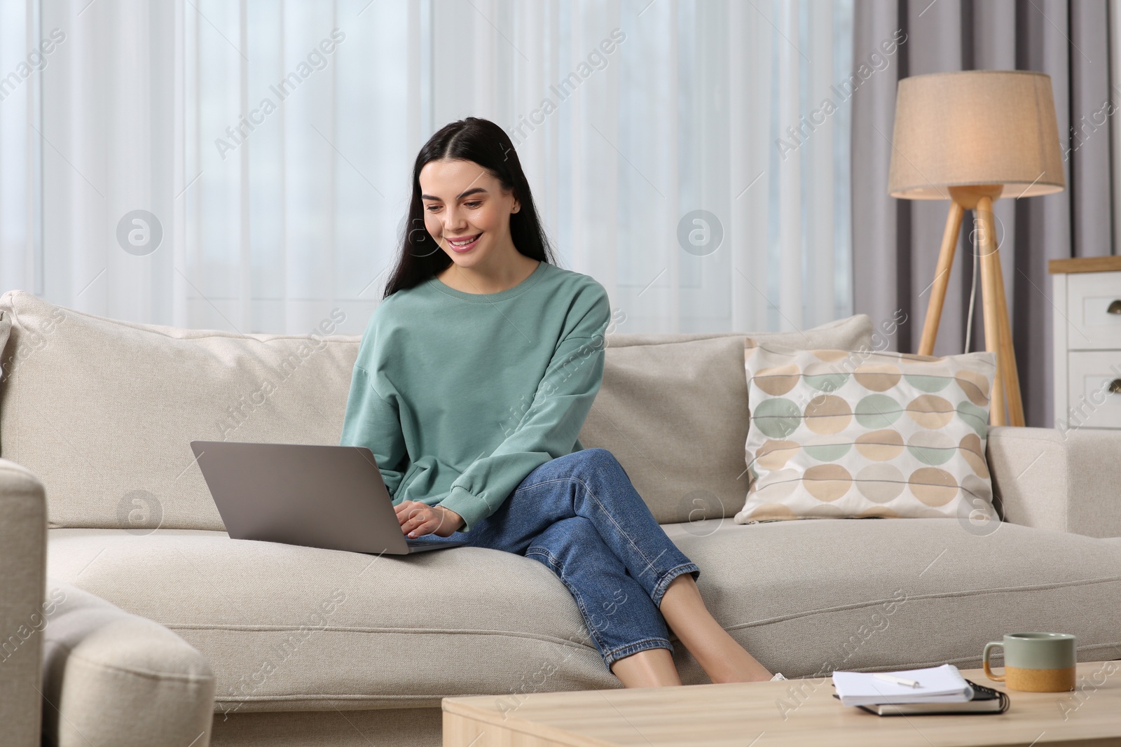 Photo of Happy woman working with laptop on sofa at home